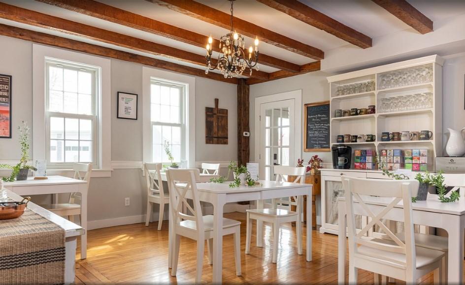 Cozy dining room with white tables, wooden floor, and a chandelier.