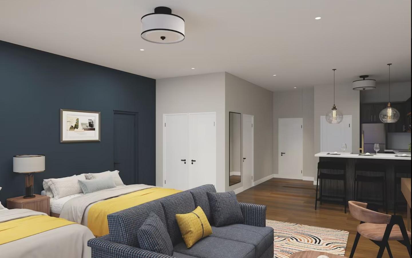 Modern hotel room with two beds, cozy seating, and a small kitchenette.