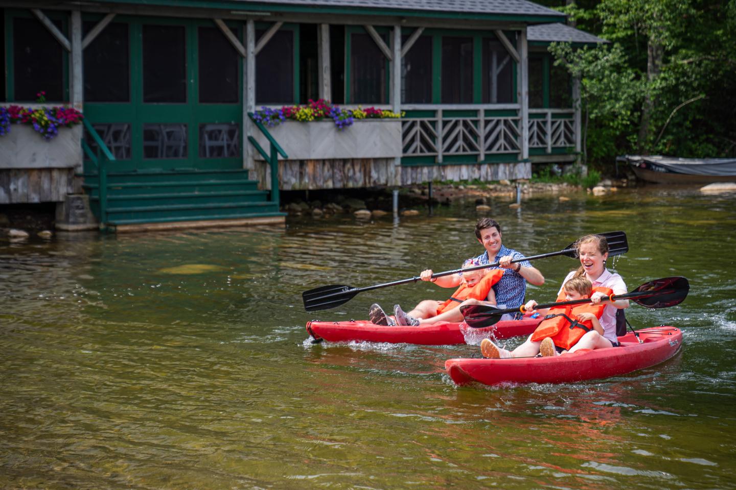 Two people kayaking on a lake near a wooden cabin.