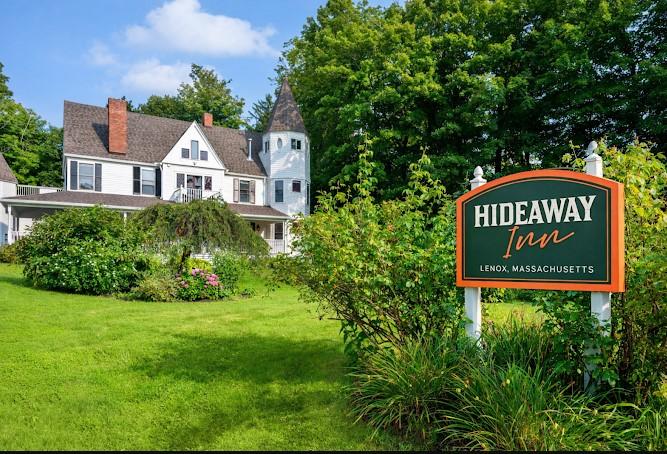Historic inn with white siding, lush gardens, and prominent sign in foreground.