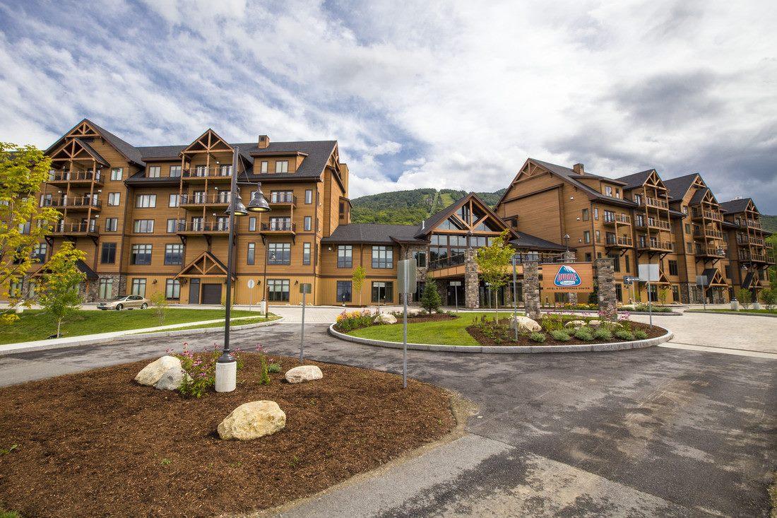 Large wooden lodge with mountains in the background. Cloudy sky above.