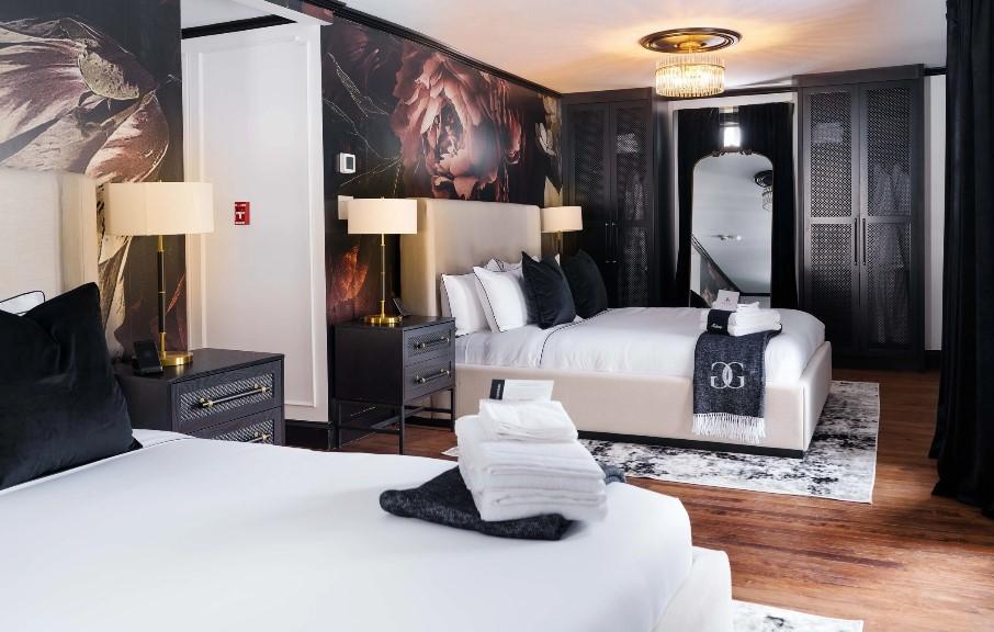 Modern hotel room with two beds, dark walls, and elegant lighting.