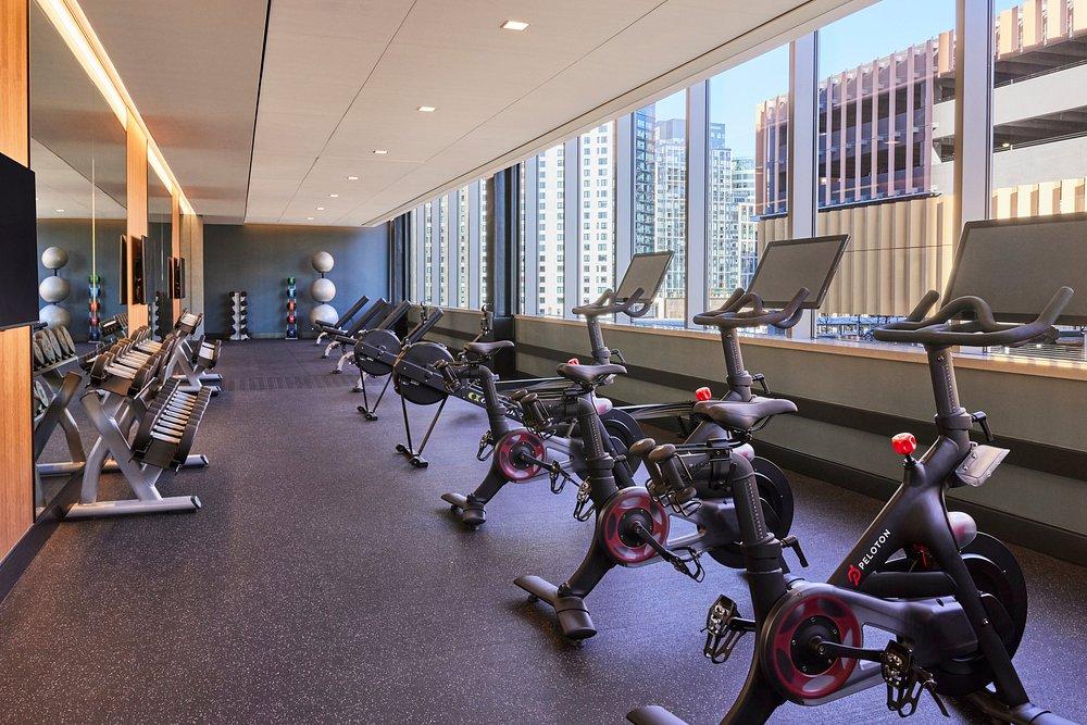 Modern gym with exercise bikes, large windows, city view, and natural light.