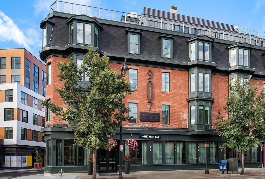 Historic red-brick hotel with large windows and green accents, trees in front.