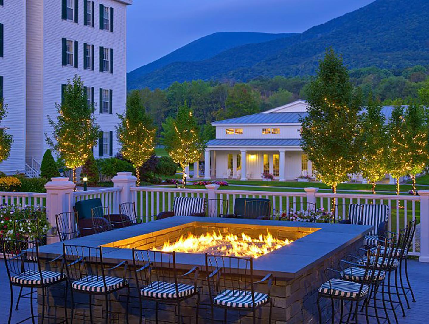 Fire pit surrounded by chairs on hotel patio, mountains in the background at dusk.