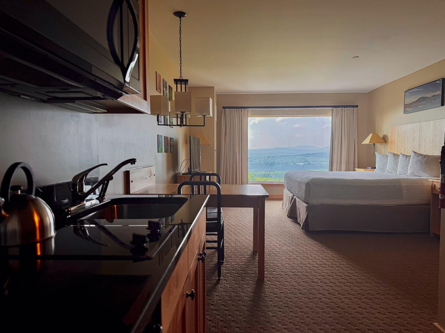 Hotel room with a bed, kitchenette, and ocean view through a large window.