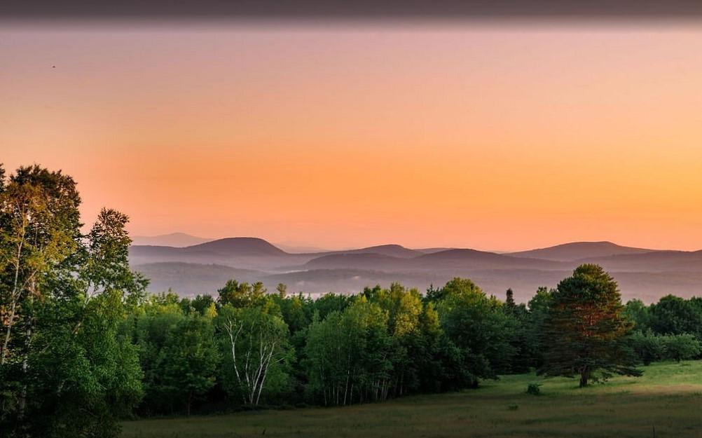 Sunset over green fields and distant hills with colorful sky.