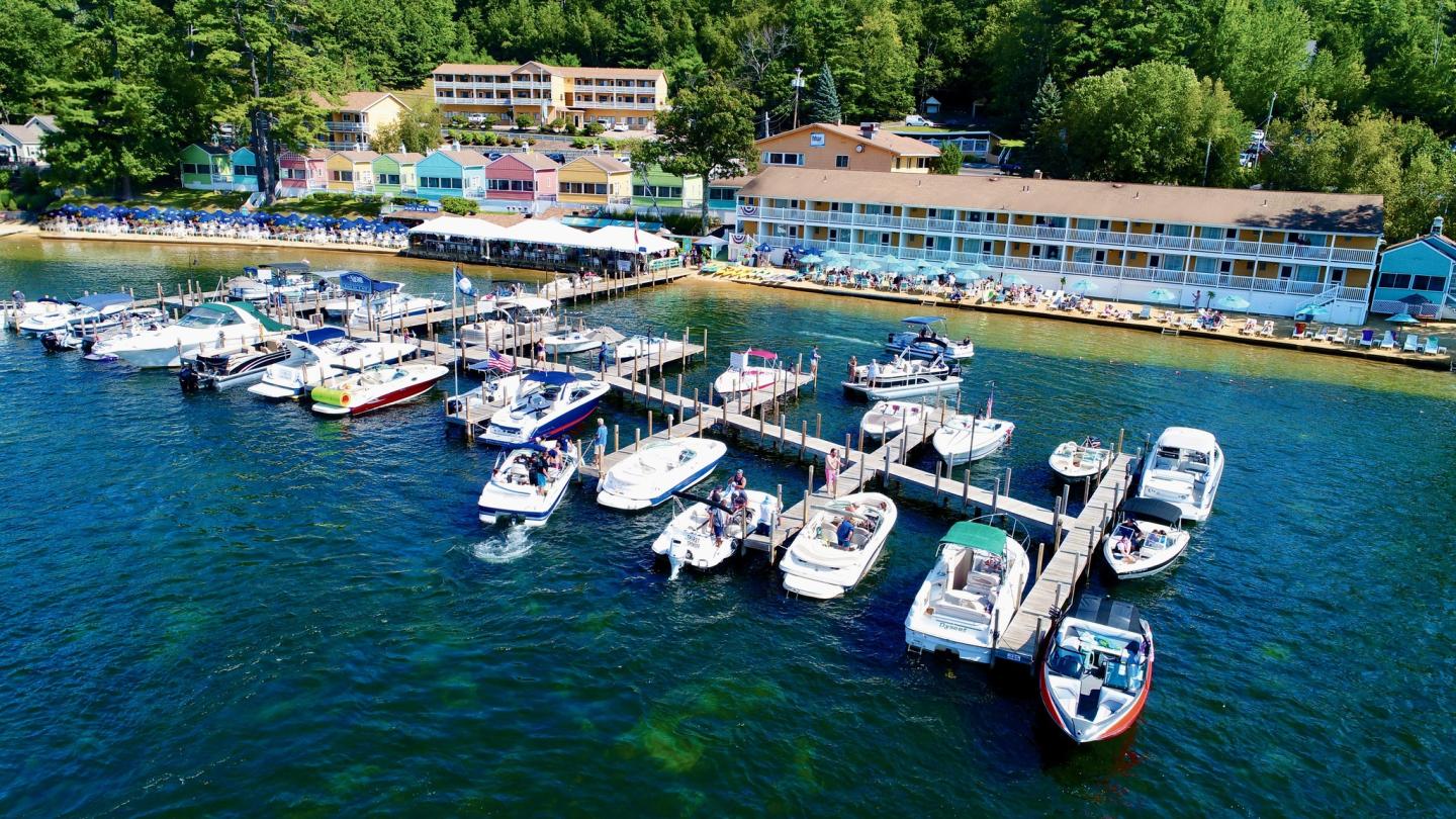 Marina with boats docked, colorful cottages and trees in background.
