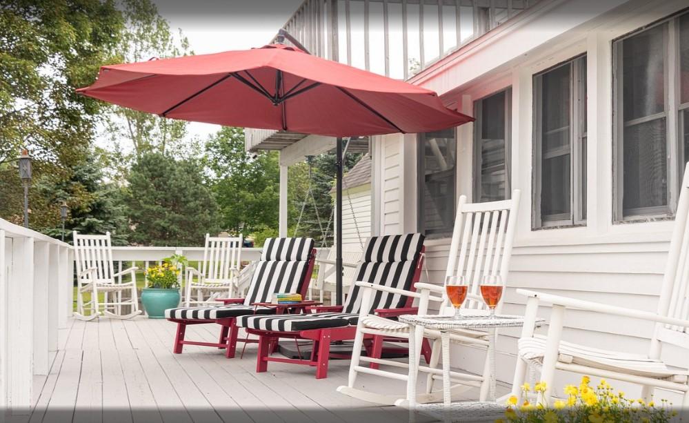 Sunny patio with chairs, red umbrella, and potted flowers.