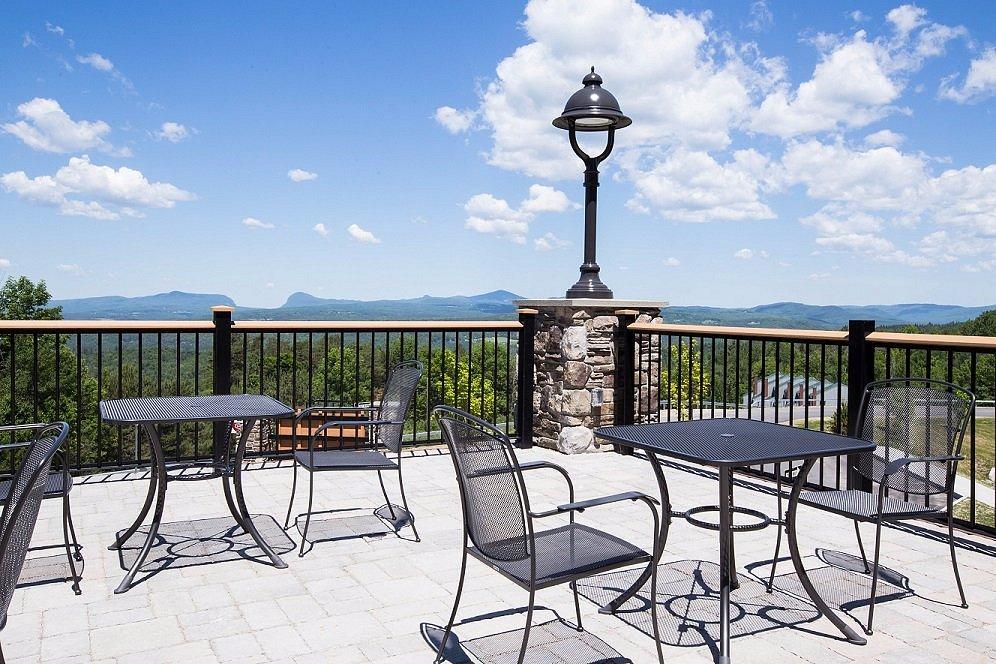 Sunny patio with empty metal tables and chairs, mountains in the background.