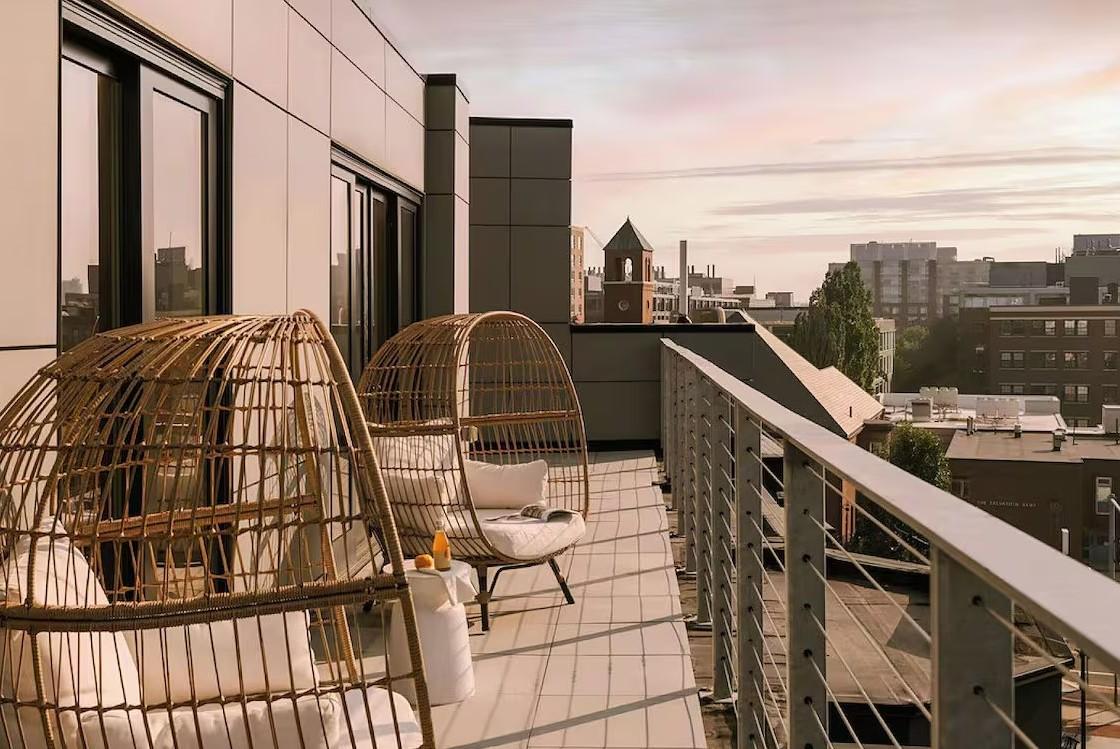 Rooftop patio with wicker egg chairs, overlooking a cityscape at sunset.