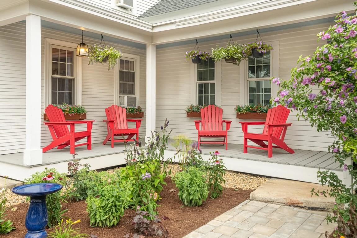 Red chairs on a porch with flowers and potted plants.