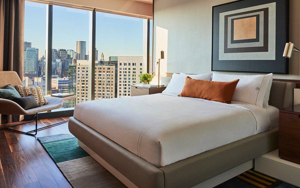 Modern hotel room with a city view, large bed, and abstract wall art.
