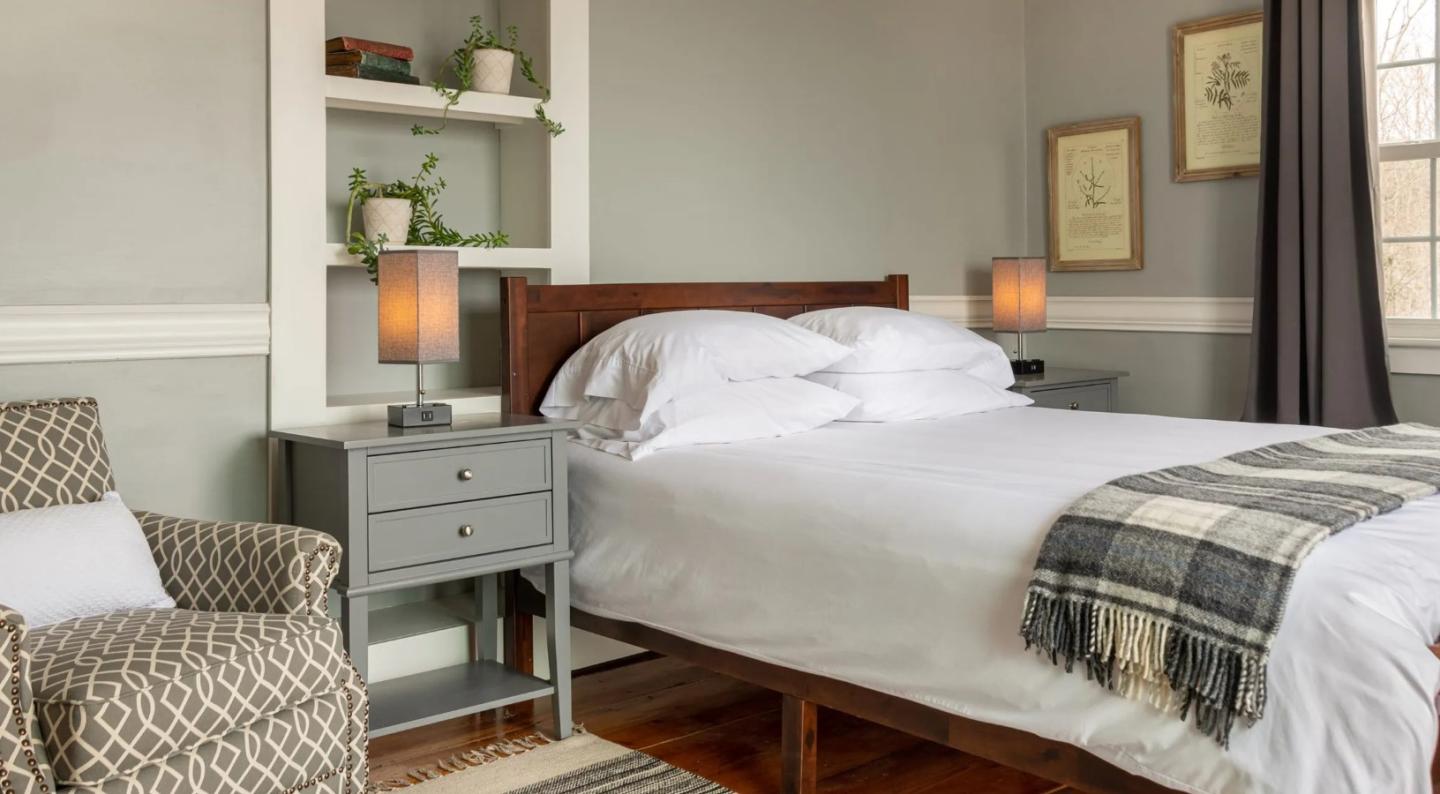 Cozy bedroom with a neatly made bed, plaid throw blanket, and bedside lamps.