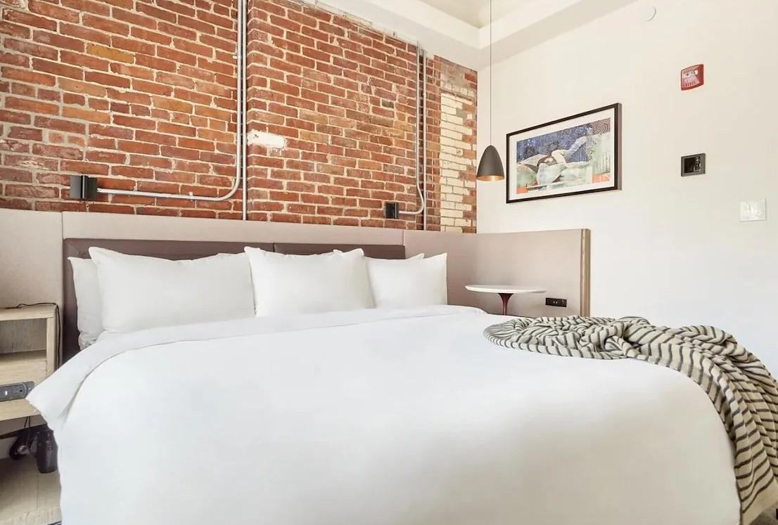 Cozy bedroom with brick wall, white bed, and framed art.