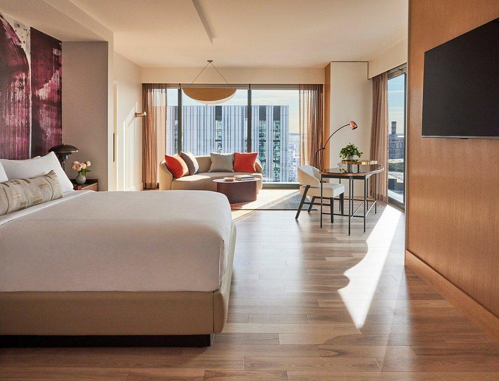 Modern hotel room with a large bed, sofa, desk, and city view.