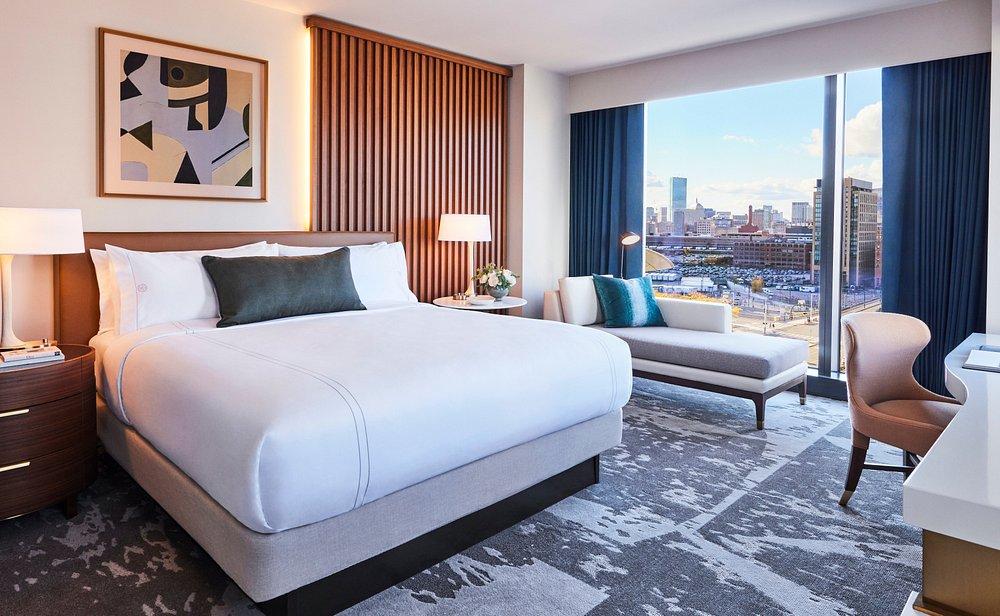 Modern hotel room with a large bed, city view, and contemporary furnishings.