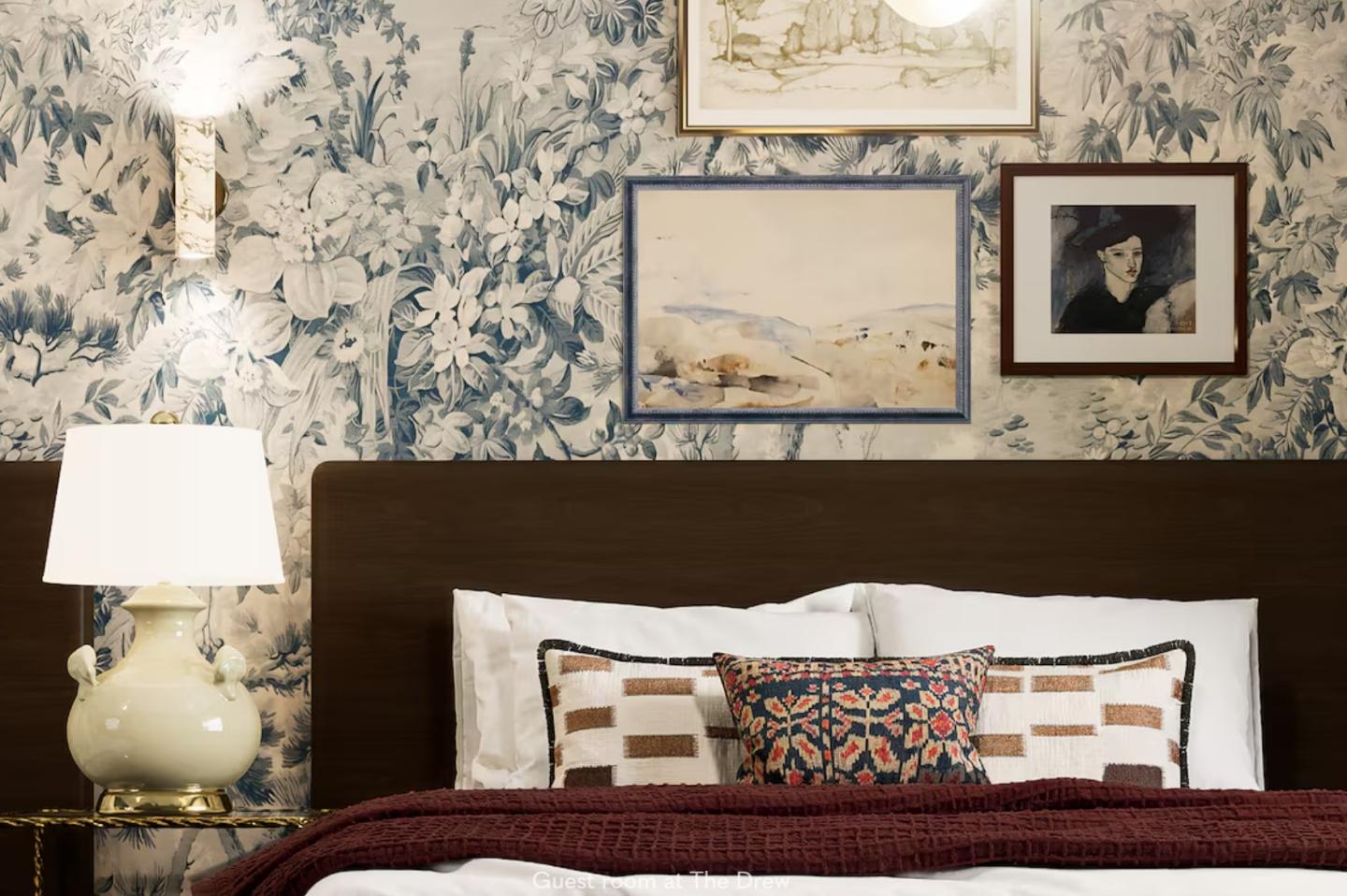 Cozy bedroom with floral wallpaper, framed art, and a neatly made bed.