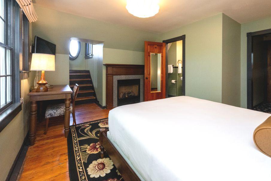 Cozy bedroom with a fireplace, desk, and large bed, natural lighting from a window.