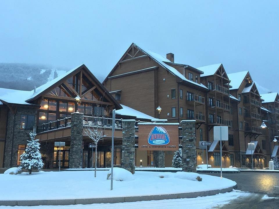 Snow-covered wooden lodge with a sign, surrounded by evergreen trees.