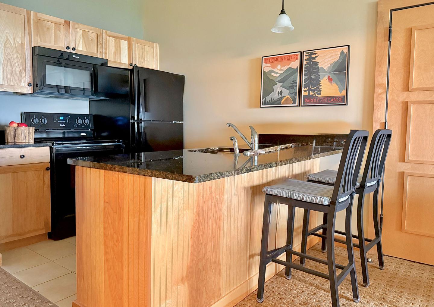 Kitchen with wooden cabinets, black appliances, and a breakfast bar with stools.