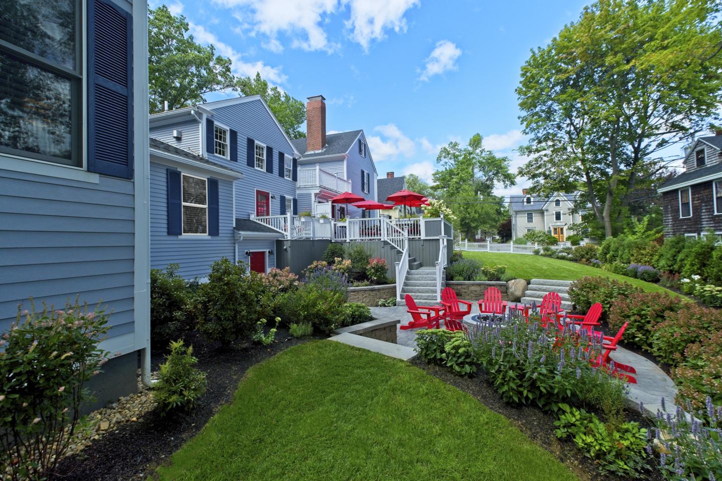 Spacious backyard with red chairs and umbrellas, surrounded by greenery and blue sky.
