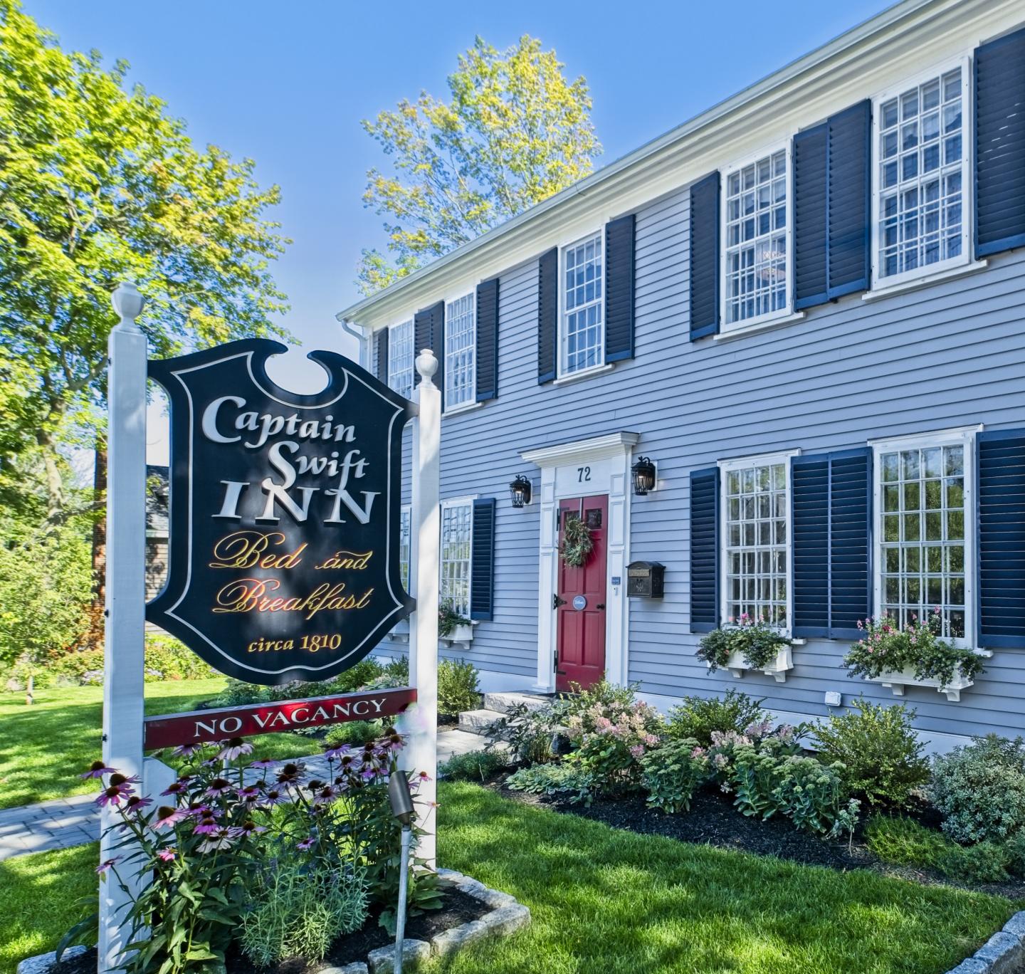 Historic inn with a red door, garden, and sign on a sunny day.