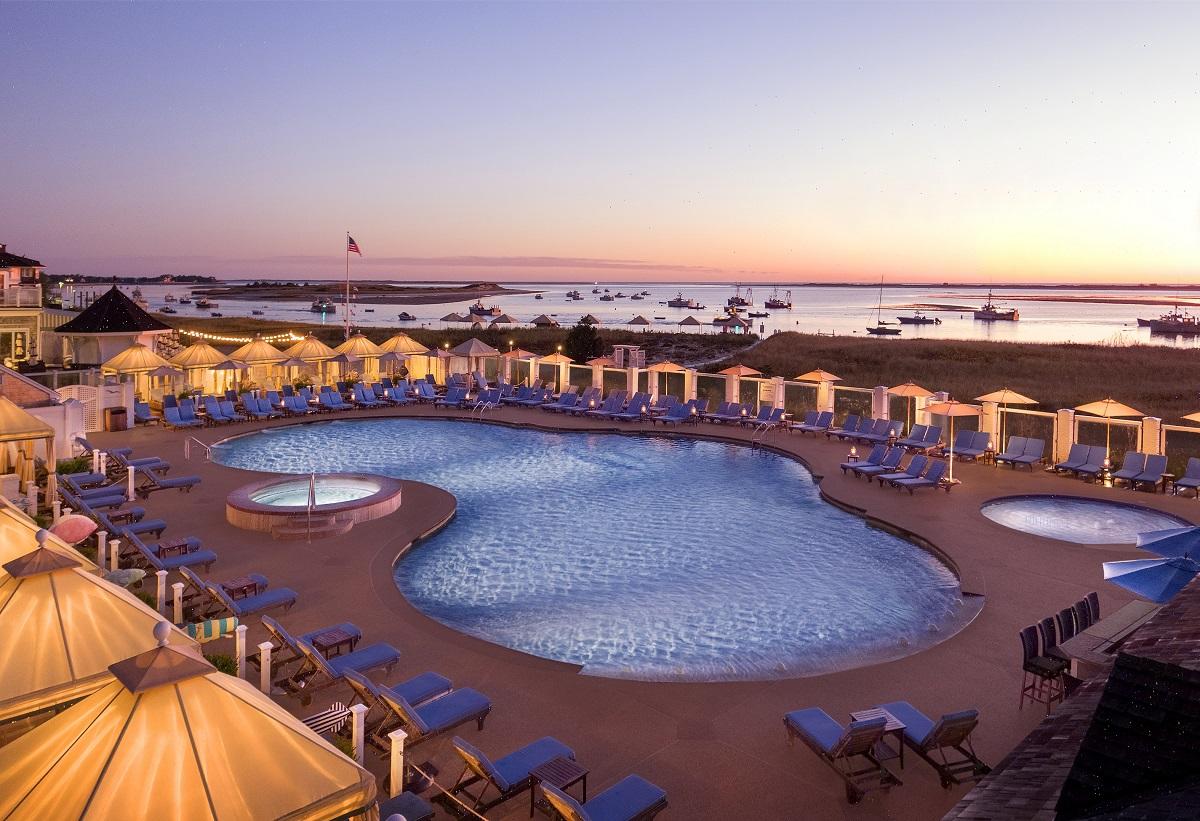 Large outdoor pool at sunset, surrounded by umbrellas and sun loungers.