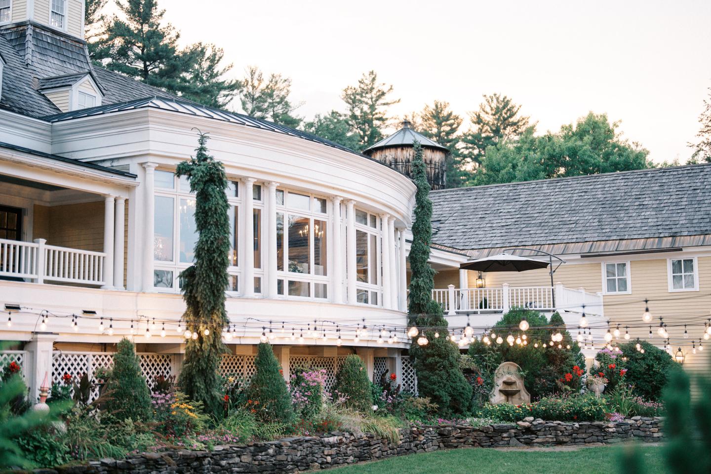 Elegant house with large windows, surrounded by a garden and string lights.