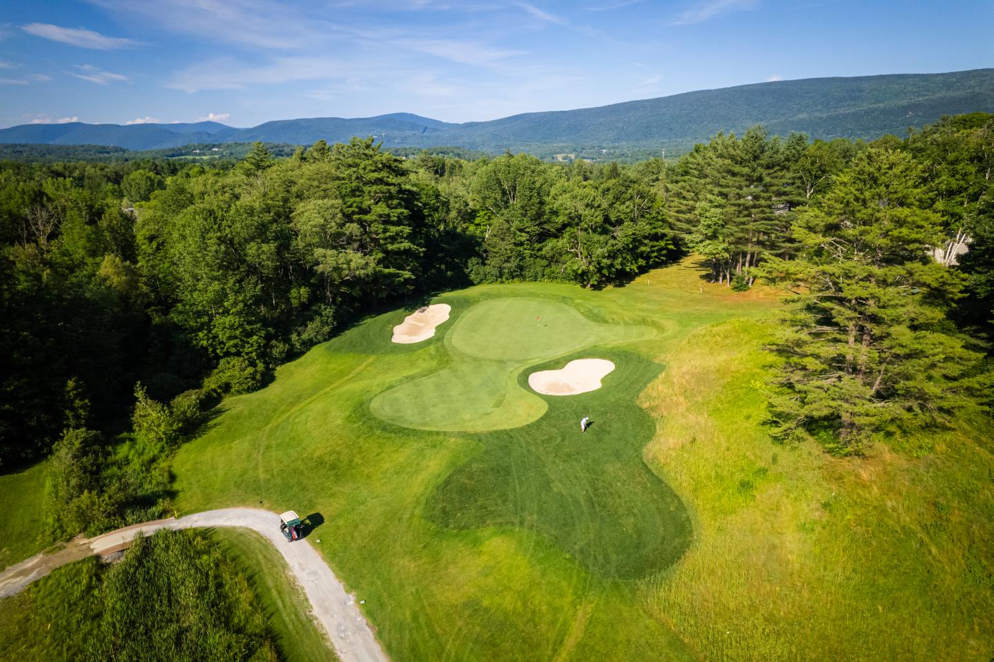 Aerial view of a golf course with green fairways and sand traps, surrounded by trees.