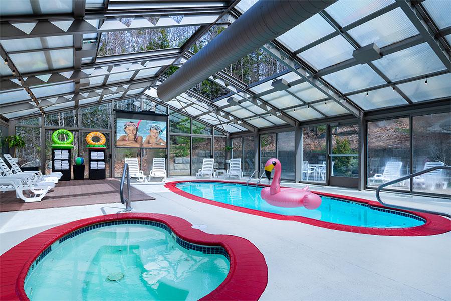 Indoor pool area with a flamingo float and loungers under a glass roof.