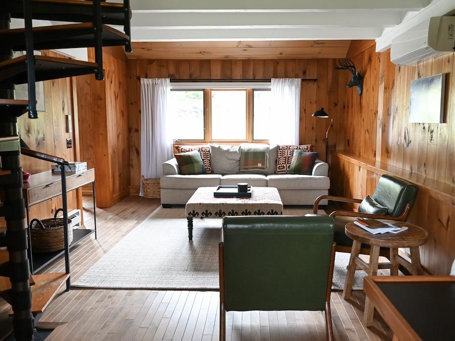 living room with wooden walls, spiral staircase, and green chairs.