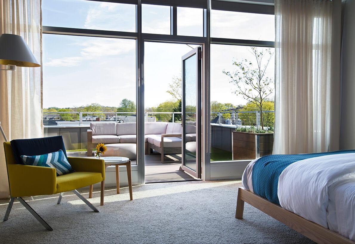 Bedroom with balcony, modern chair, and open glass doors to outdoor seating.