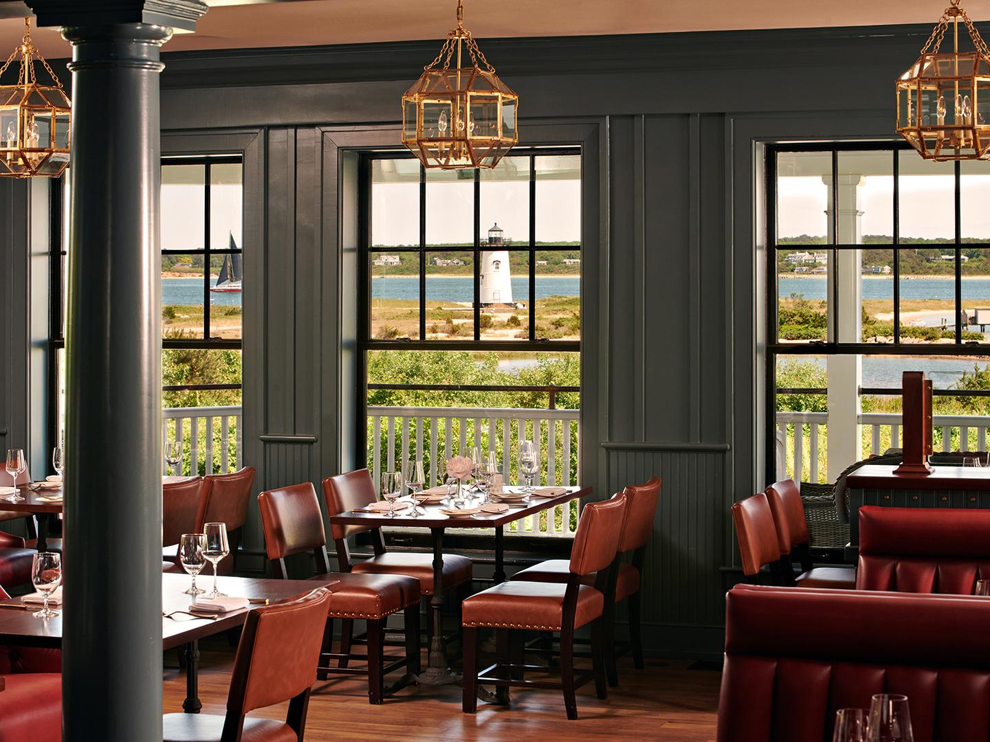 Cozy restaurant interior with large windows and a view of a lighthouse.