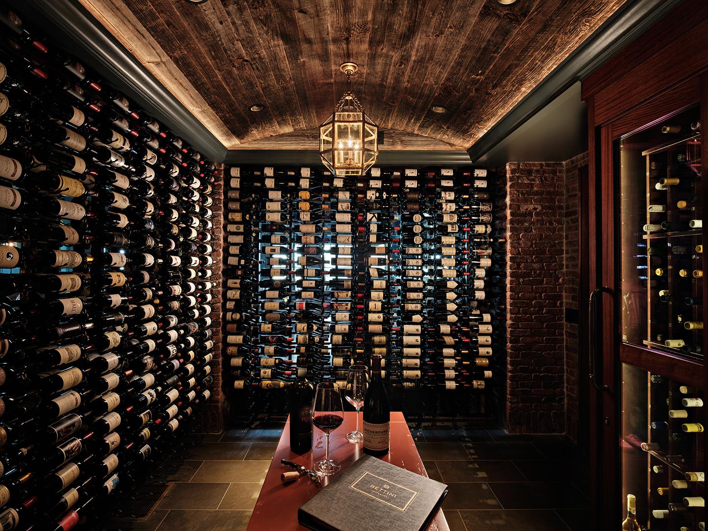 Dimly lit wine cellar with shelves of wine bottles and a table with open bottles.