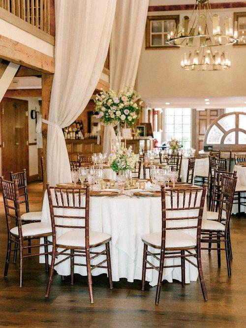 Elegant dining area with round table, floral centerpiece, wooden chairs, and chandeliers.