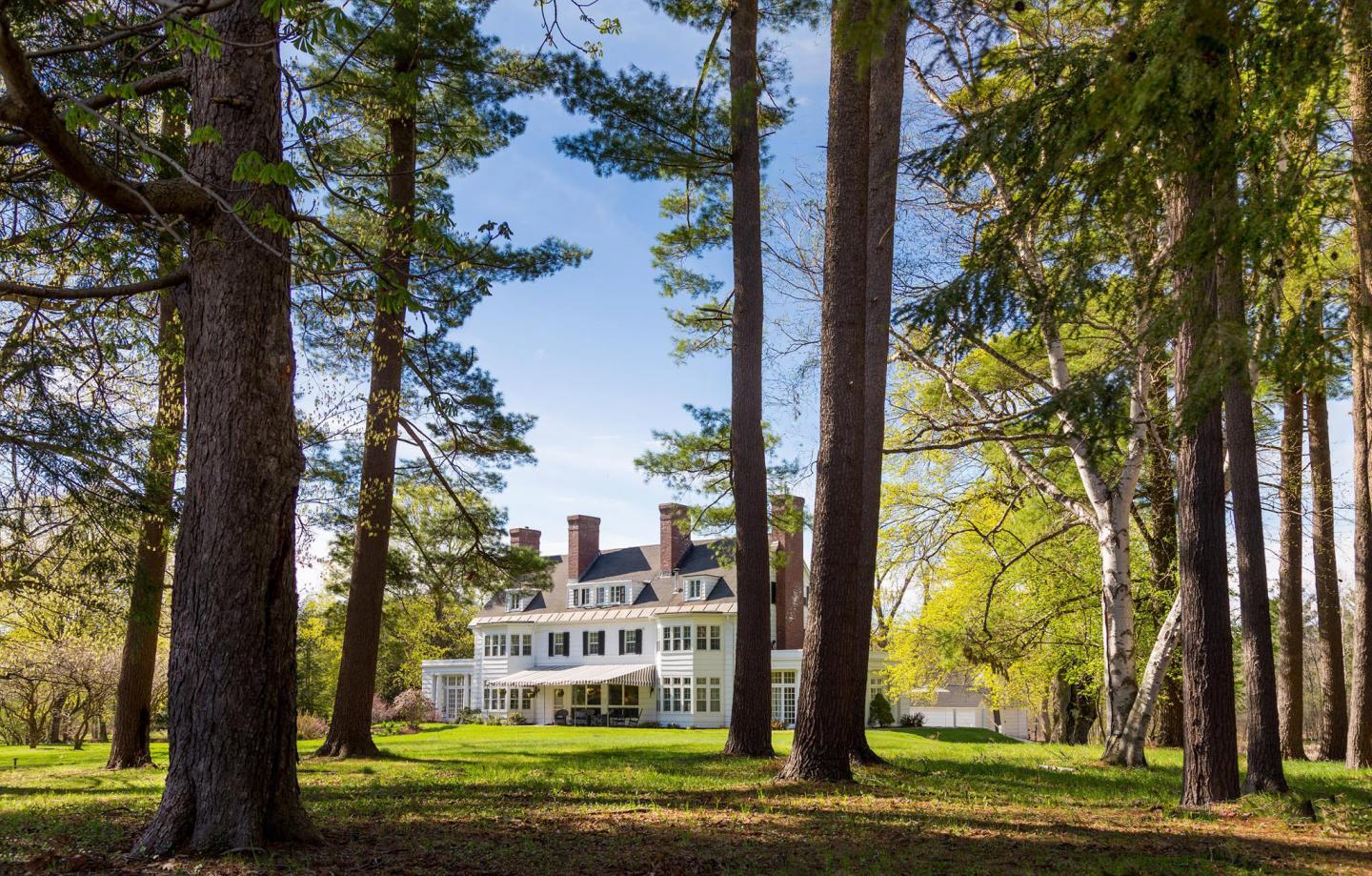 Grand white house surrounded by tall trees, under a clear blue sky.