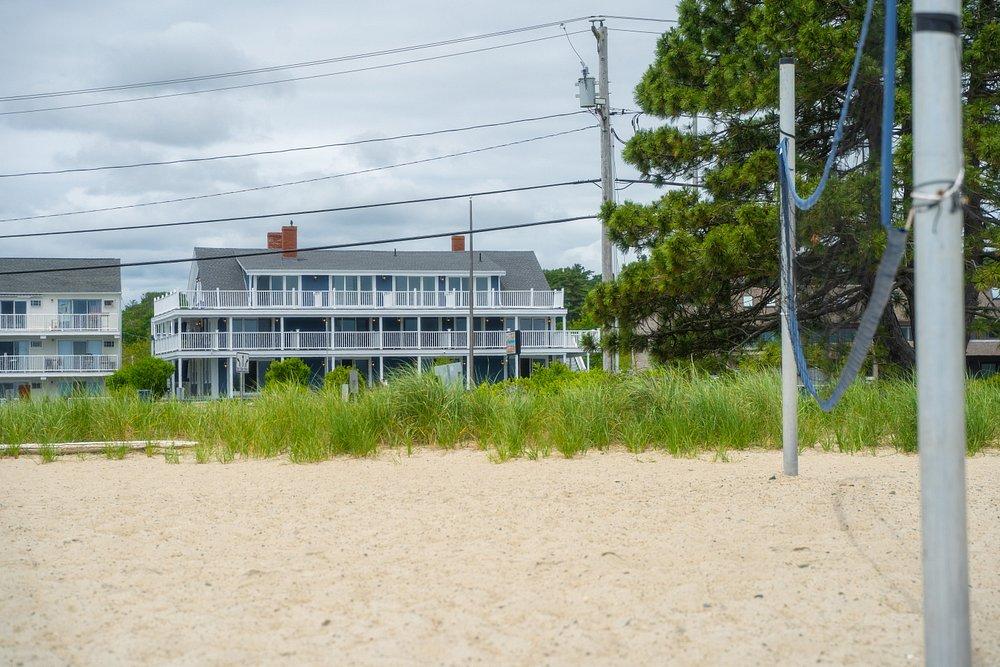 Sandy volleyball court with grass and buildings in the background.