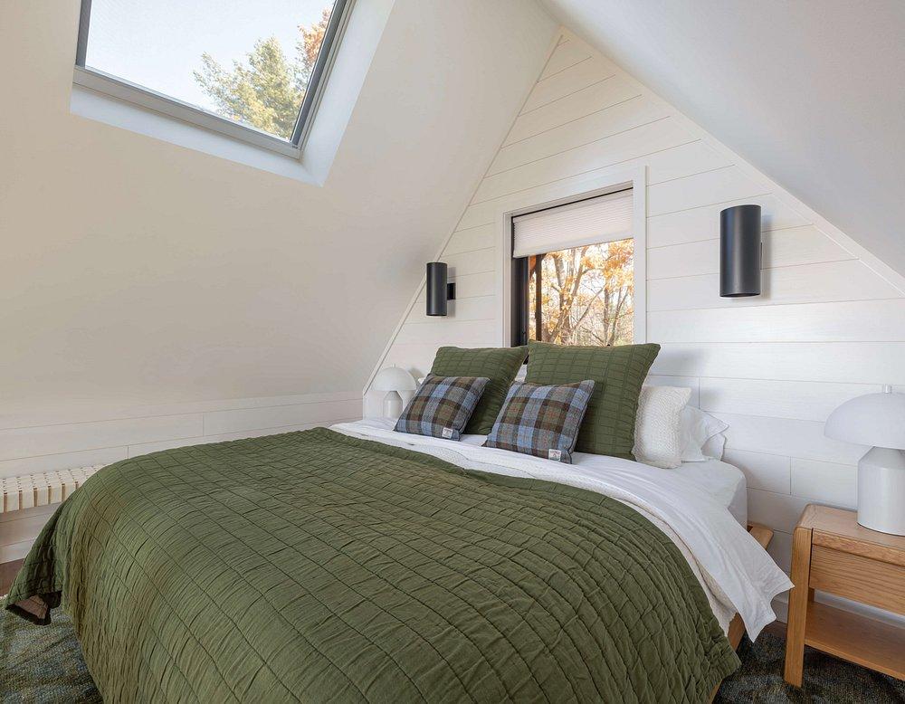 Cozy attic bedroom with green bedding, skylight, and small window.