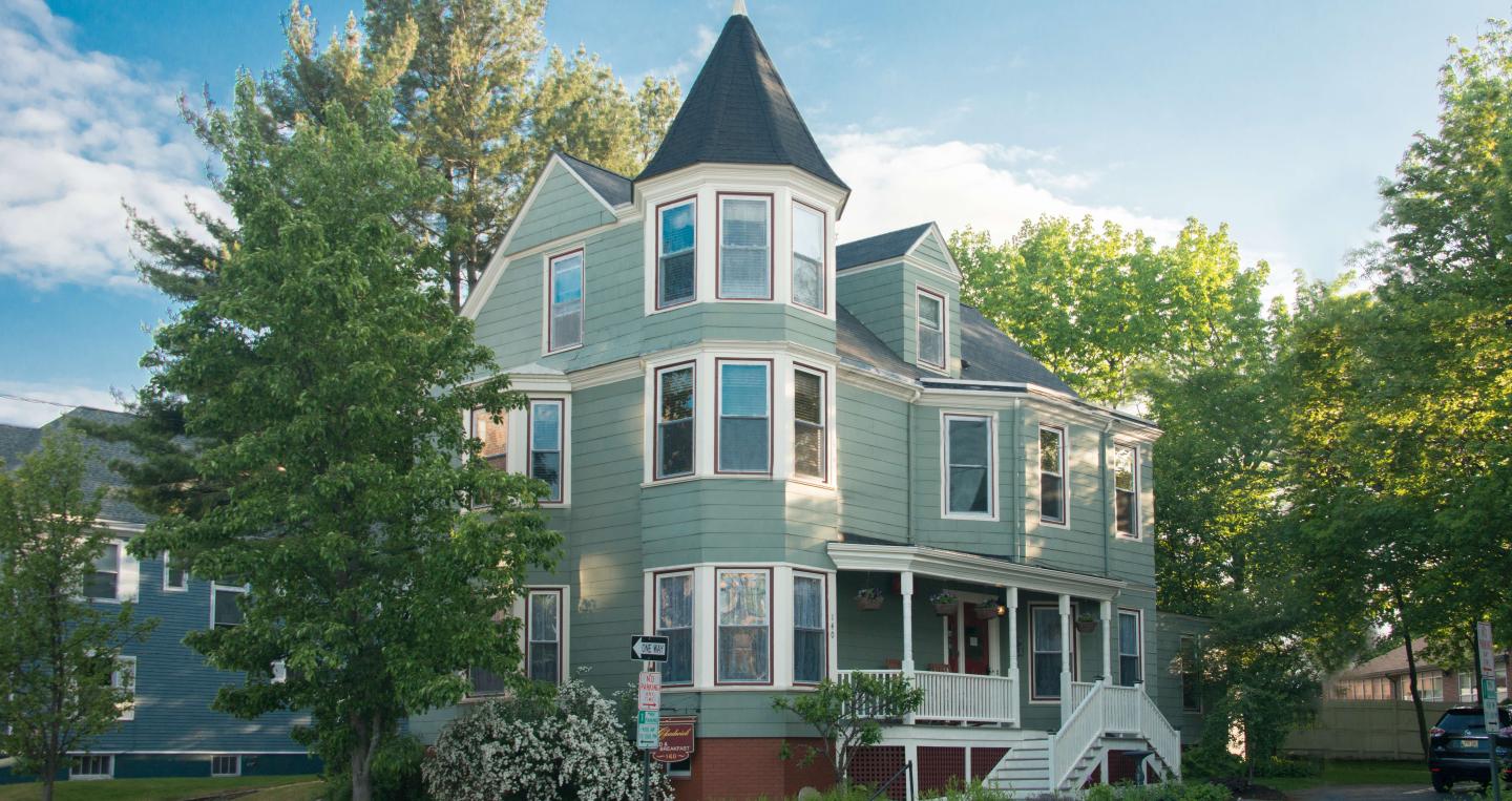 Victorian-style house with green siding, large trees, and a small staircase.