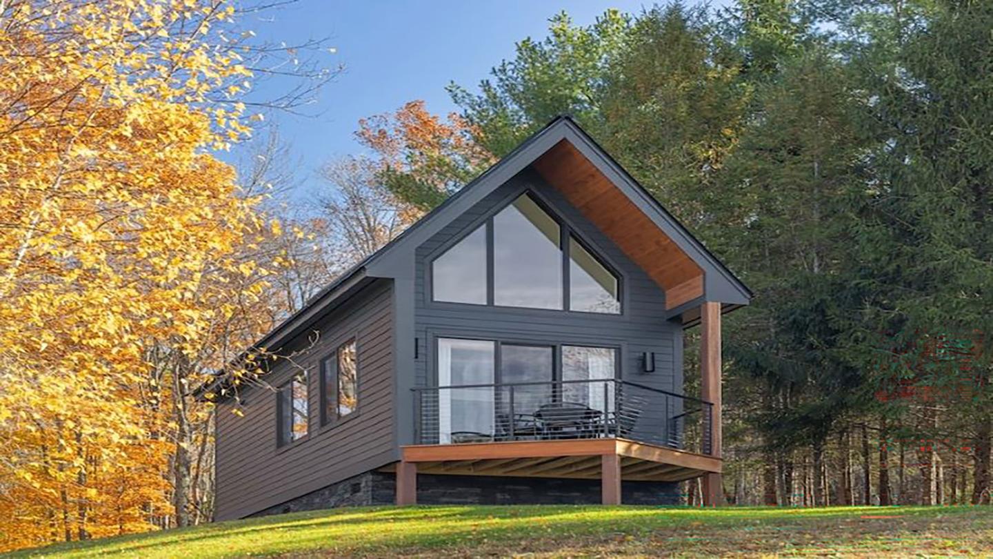 Modern cabin with large windows, surrounded by autumn trees.