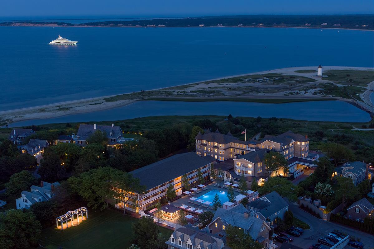 Aerial view of seaside resort at dusk, lights glowing, with ocean and ship in the background.