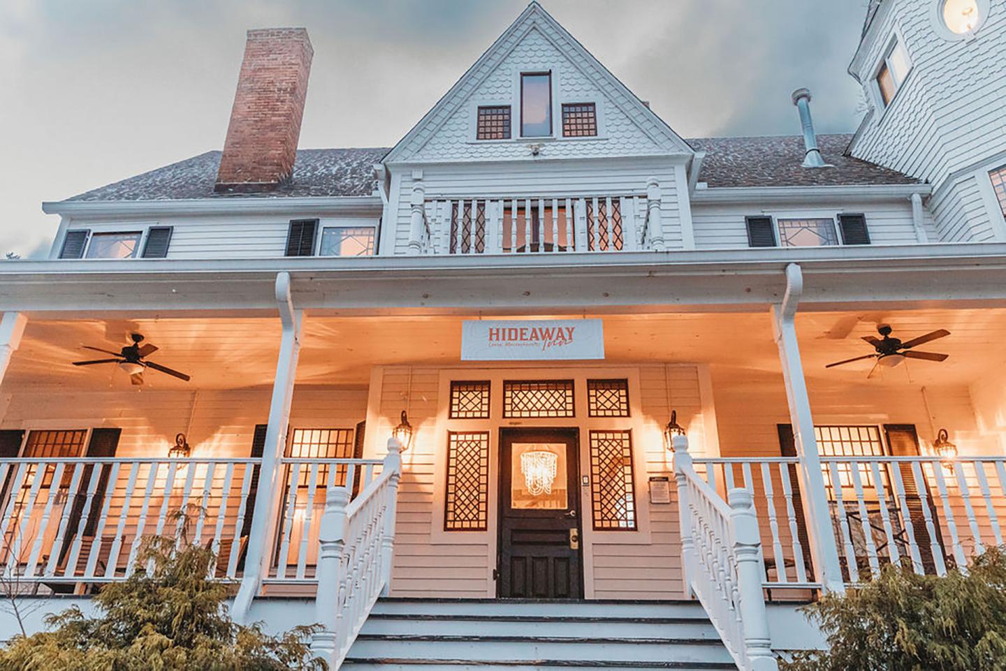 Warmly lit historic building with large porch and chimney.