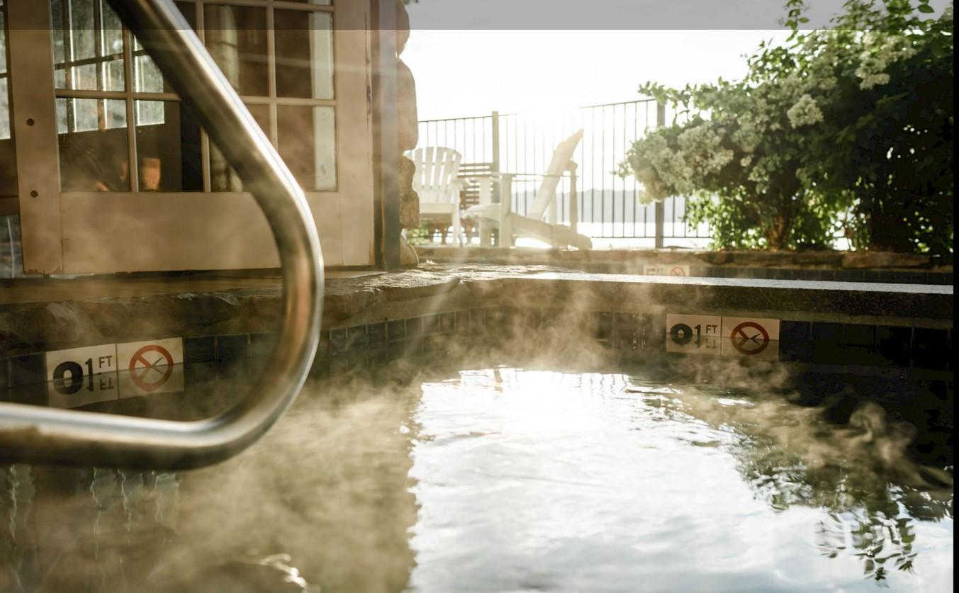 Steaming hot tub with metal railing, plants in background.