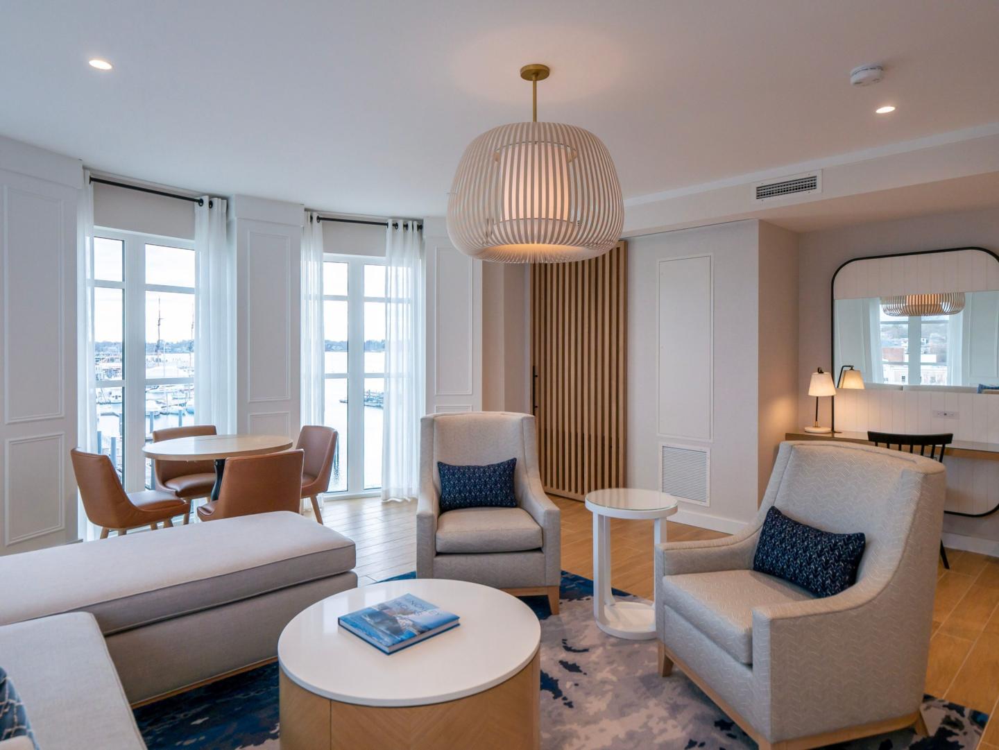 Modern living room with light furniture, large windows, and a pendant light.