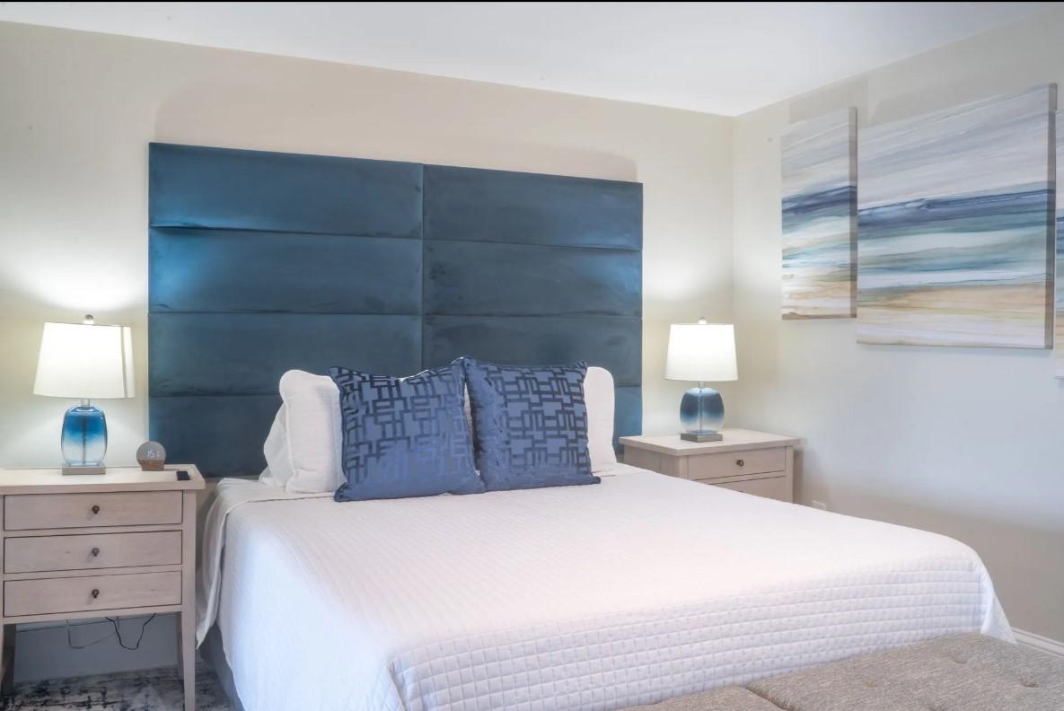 Modern bedroom with blue headboard, lamps, and abstract paintings.