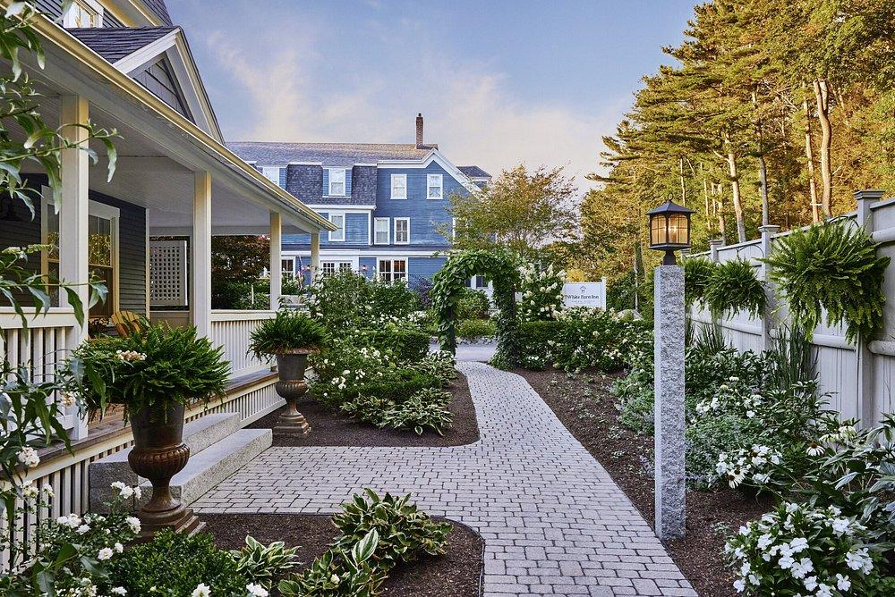 Brick path and greenery in a manicured garden beside a blue house.