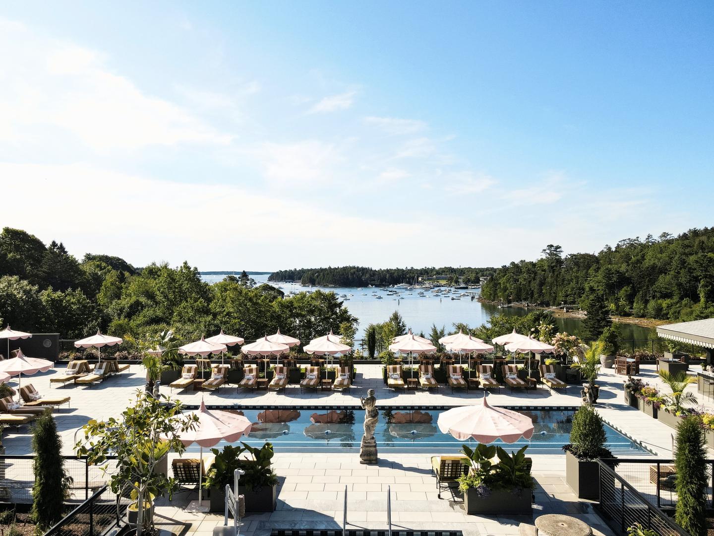 Luxurious pool area with umbrellas, overlooking a lake and surrounded by trees.
