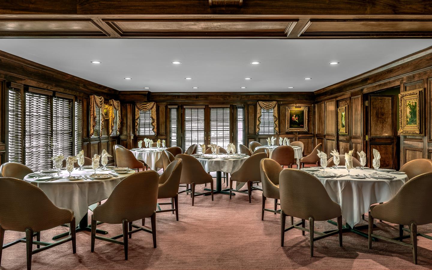 Elegant restaurant with round tables, set for dining, surrounded by wood-paneled walls.