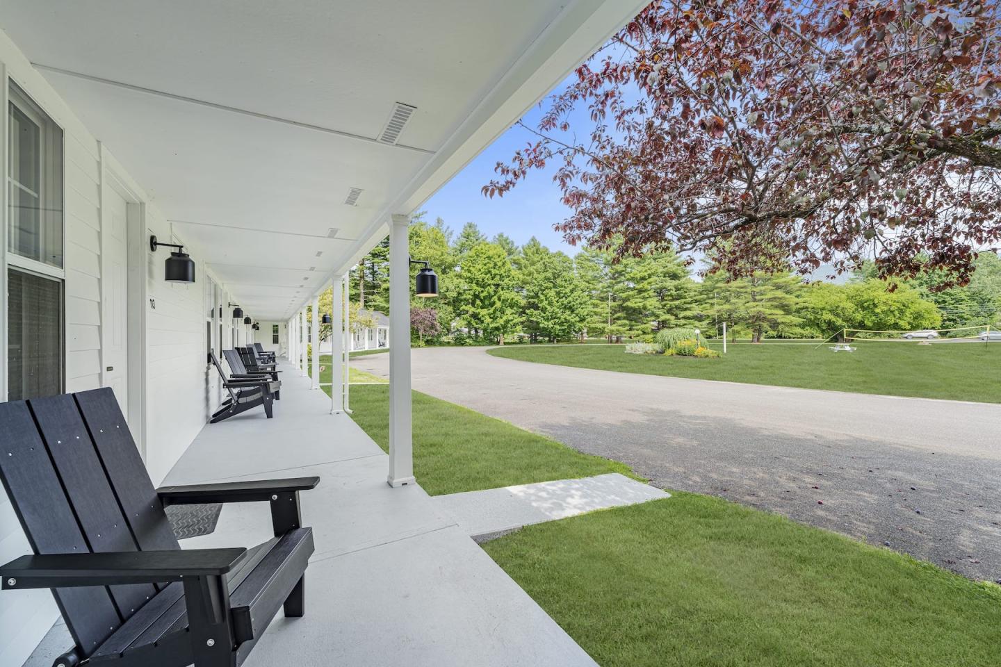 Covered porch with wooden chairs overlooking a grassy area and trees.